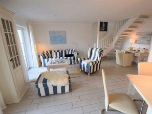 A spacious living room with striped armchairs, a sofa, and a coffee table. A staircase leads to an upper level.
