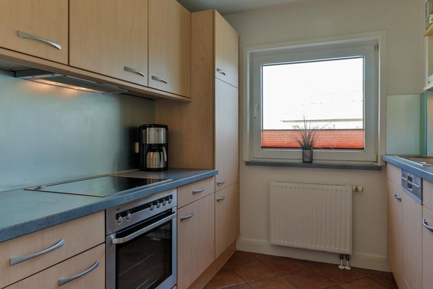 A compact kitchen with light wood cabinets, a built-in oven, a coffee maker on the counter, and a window with a view of the outside.