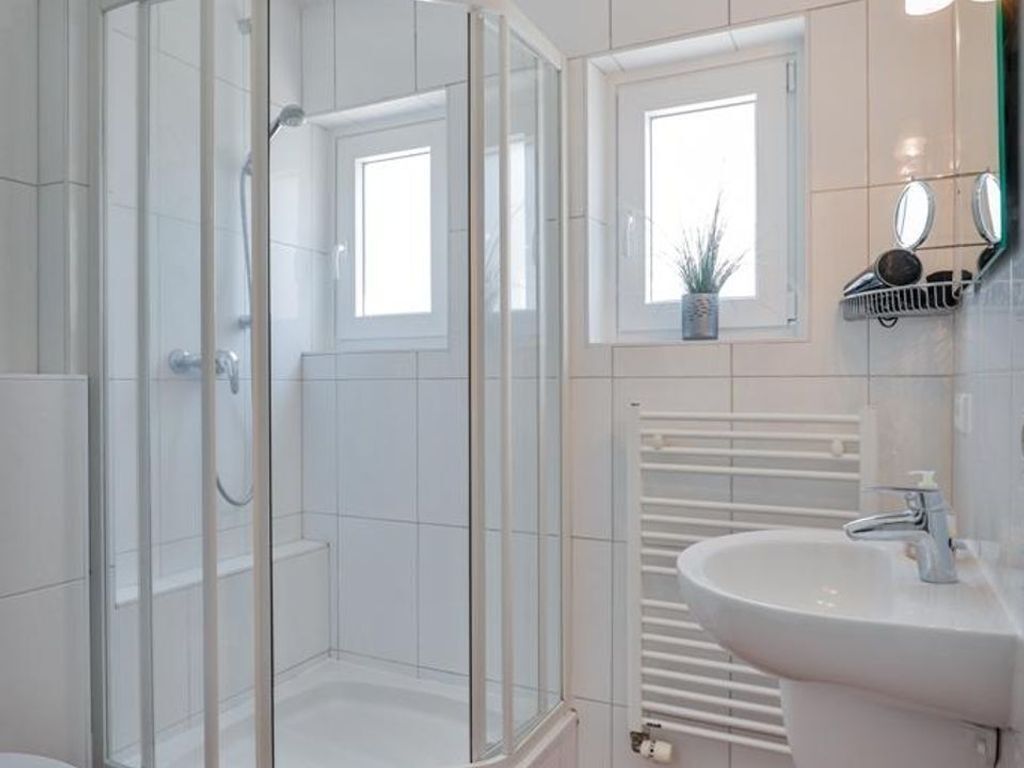 Un baño moderno con ducha de vidrio, lavamanos blanco y una pequeña ventana con una planta.