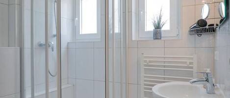 Un baño moderno con ducha de vidrio, lavamanos blanco y una pequeña ventana con una planta.
