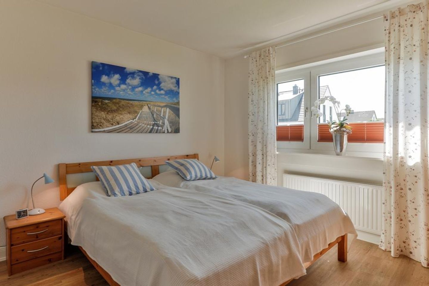 Een slaapkamer met een houten bed, twee kussens, een nachtkastje, een lamp en een raam met gordijnen.