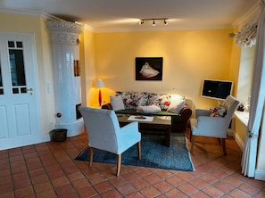 Ein Wohnzimmer mit einer Couch, zwei Sesseln, einem Couchtisch, einem Fernseher und einem Gemälde an der Wand.