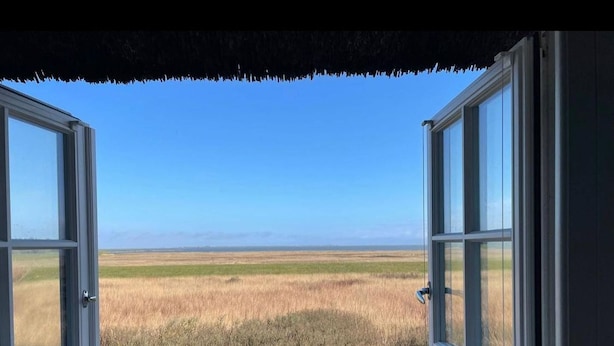 An open window with a view of a flat landscape and a clear blue sky.