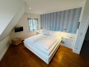 A bedroom with a large bed, a TV mounted on the wall, a window with curtains, and a striped wall. - "Carpe Diem" RH/2D Vacation Home - Reethüs am Watt "Carpe Diem" (Sylt)