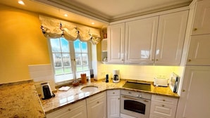 A kitchen with white cabinets, a granite countertop, a built-in oven, and a window with curtains.