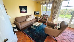A living room with a sofa, armchair, and a glass coffee table. There is a television and a window with curtains. - "Carpe Diem" RH/2D Vacation Home - Reethüs am Watt "Carpe Diem" (Sylt)