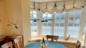 A dining room with a round table, chairs, a vase with flowers, and a window with curtains.