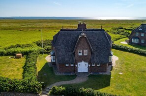 A large, thatched-roof house with a symmetrical facade, a central entrance, and a well-maintained lawn. - "Carpe Diem" RH/2D Vacation Home - Reethüs am Watt "Carpe Diem" (Sylt)