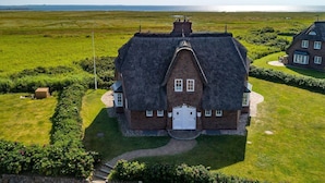 A large, thatched-roof house with a symmetrical facade, a central entrance, and a well-maintained lawn.