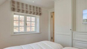 A bedroom with two beds, a window with a checkered valance, and a white wardrobe. - Dünen Hüs II HO/34b - Dünen Hüs II (Sylt)