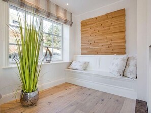 A room with a wooden bench, a potted plant, and a window with blinds.