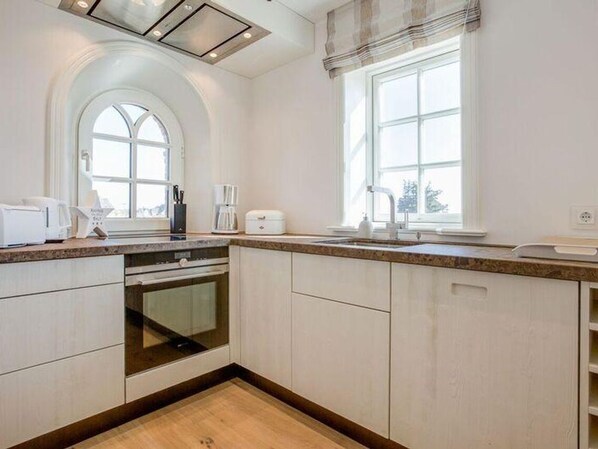 A modern kitchen with white cabinetry, a built-in oven, a large window, and a view of the outdoors.