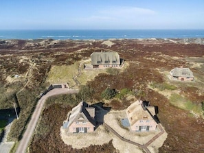 A coastal property with multiple buildings, including a main house and several smaller structures, surrounded by natural terrain and a view of the sea.