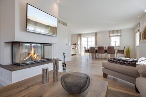 Un salon moderne avec une cheminée, un coin repas et une cuisine en arrière-plan.