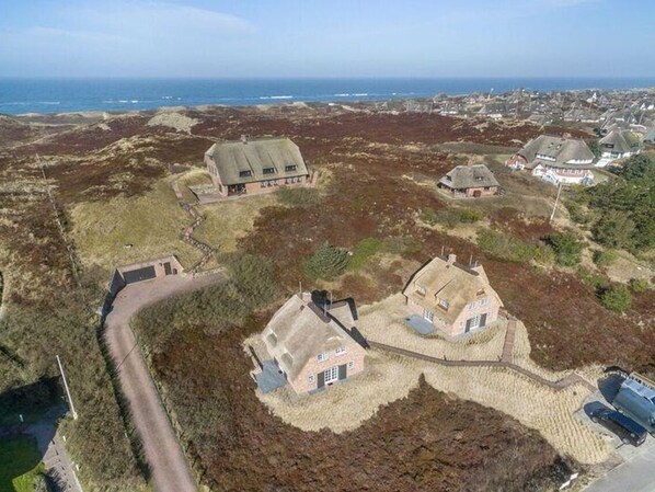 Une vue aérienne d’un village côtier, avec des maisons entourées d’un paysage naturel, un ciel dégagé et une vue sur la mer.