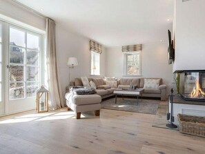 A modern living room with a sofa set, a coffee table, a fireplace, and large windows.