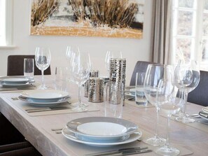 Une table à manger dressée avec des assiettes, des verres et des couverts, et un tableau en arrière-plan.