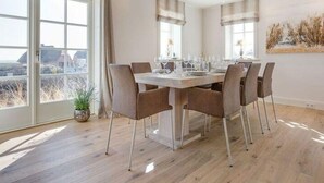 A dining area with a large table set for six, surrounded by six chairs. - Dünen Hüs II HO/34b - Dünen Hüs II (Sylt)
