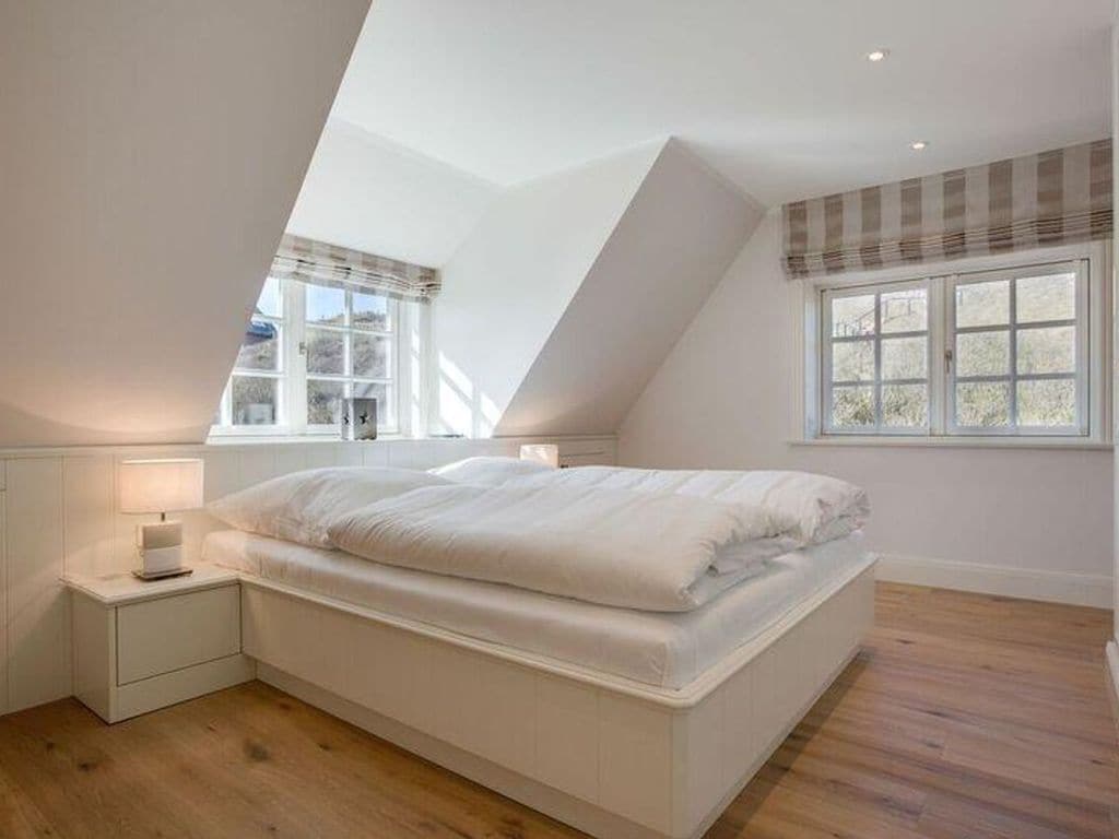Ein Schlafzimmer mit schrägen Wänden, einem Bett, einem Nachttisch und einem Fenster mit Blick.