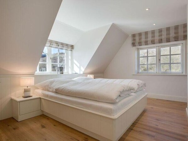 A bedroom with a sloped ceiling, a bed, a nightstand, and a window with a view.