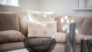 A modern living room with a beige sofa, star-patterned cushions, and a decorative bowl on the coffee table. - Dünen Hüs II HO/34b - Dünen Hüs II (Sylt)