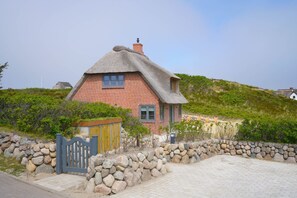 Et hus med stråtækt tag, murstensfacade, en stenvæg og en træport.