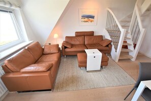 Un espacio habitable compacto con un sofá de cuero marrón, una mesita auxiliar blanca y una escalera que sube a un nivel superior.