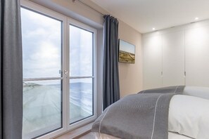 Une chambre d’hôtel avec une grande fenêtre, un lit avec une literie grise, un tableau au mur et une armoire.