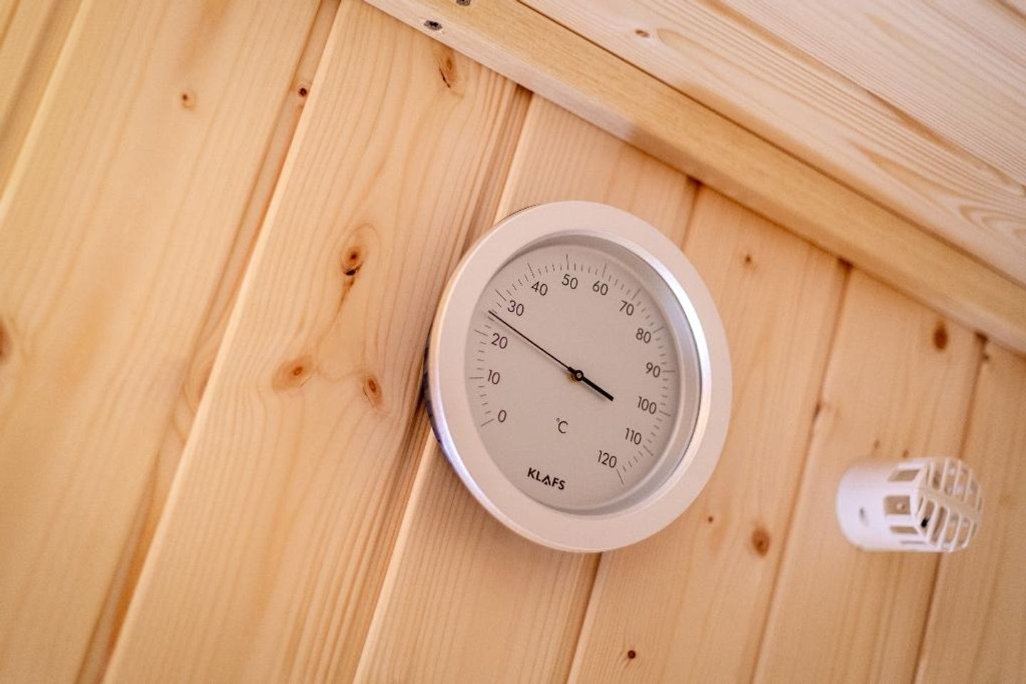 A white wall-mounted thermometer with a wooden background.