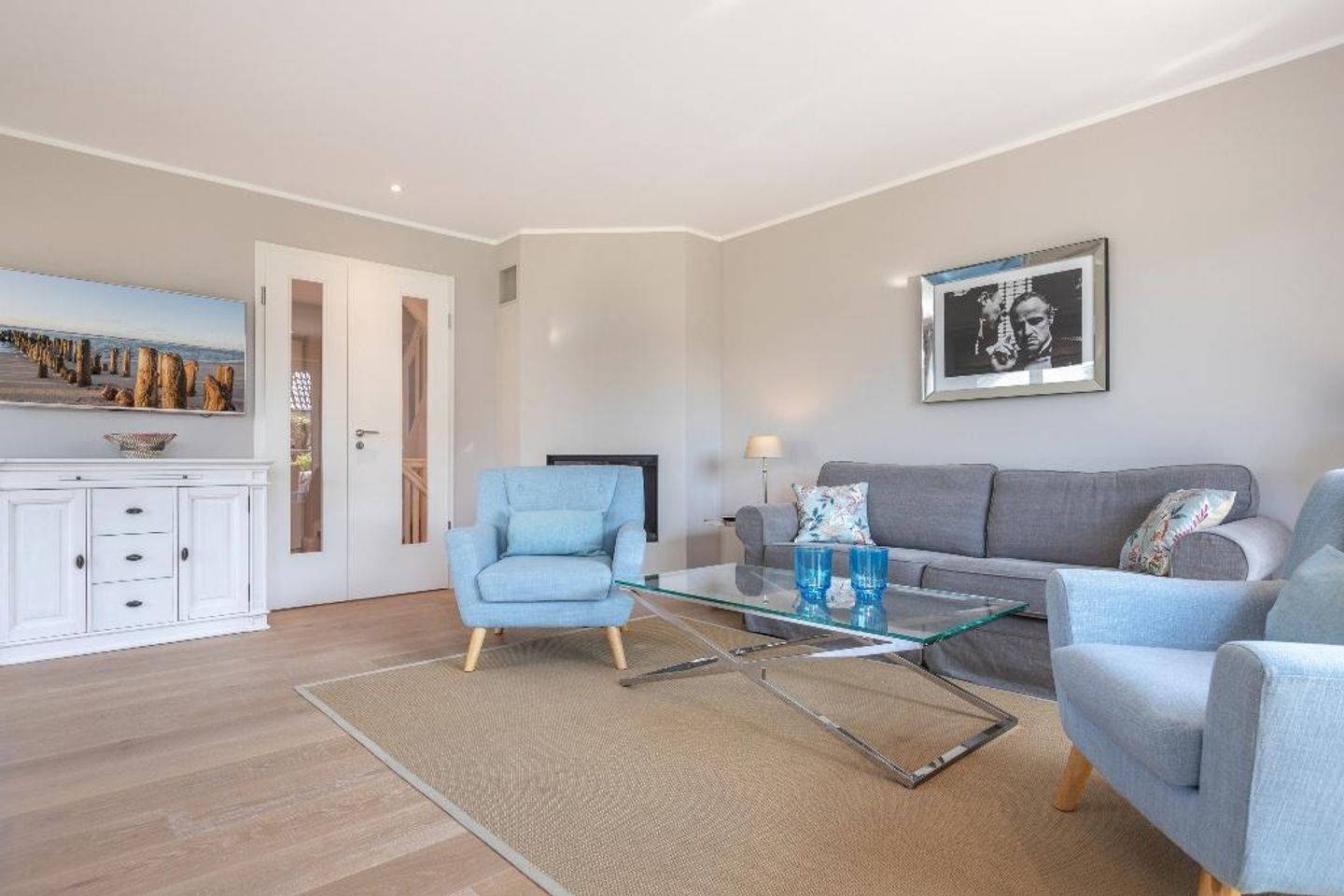 A modern living room with a sofa, armchair, glass coffee table, and a painting on the wall.