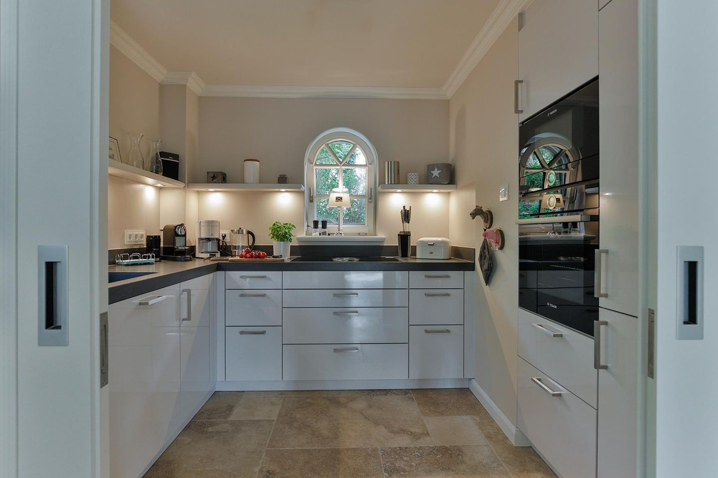 A modern kitchen with white cabinets, a central island, and a large window with a view of greenery.