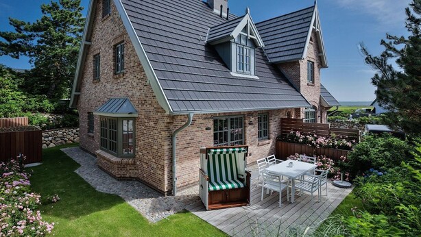 A two-story house with a sloped roof, brick exterior, and a deck with outdoor furniture. - "Raanwaikoje" RA/14B - Raanwaikoje (Sylt)