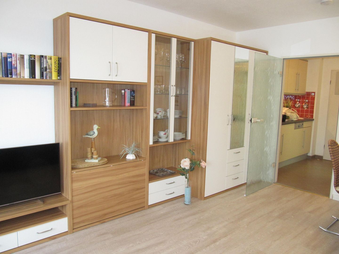 Ein Wohnzimmer mit Flachbildfernseher, Holzausbau, einer Glaskabine und einem Essbereich mit roter, gefliester Wand.