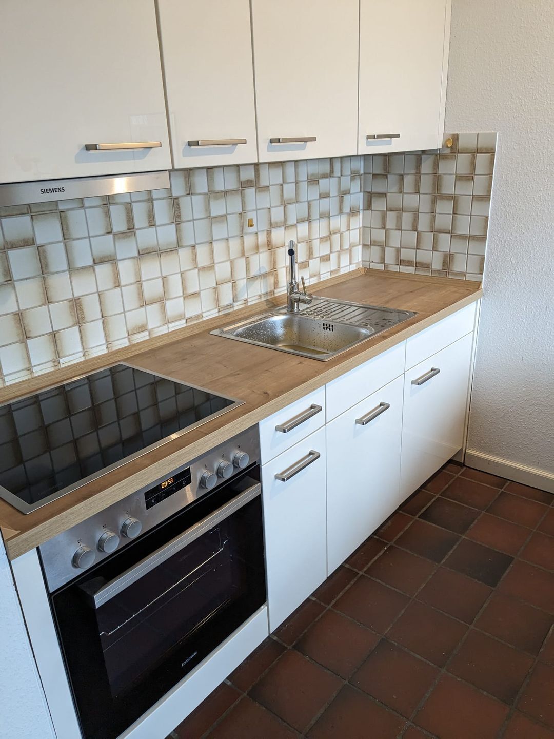 Eine moderne Küche mit weißen Schränken, einer Edelstahl-Spüle, einem schwarzen Backofen und einer Holz Arbeitsplatte.