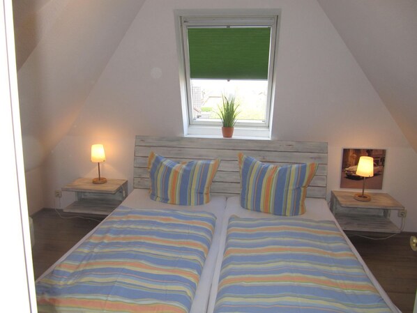 Ein Schlafzimmer mit zwei Betten, gestreifter Bettwäsche, einem Fenster mit grüner Jalousie und zwei Nachttischlampen.