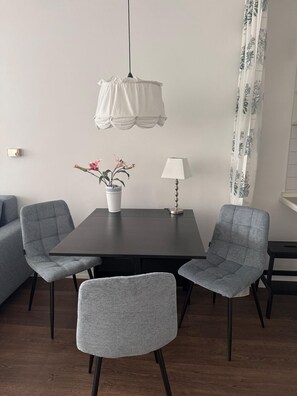 En matplats med ett mörkt träbord, två grå stoppade stolar, en vit bordslampa, en krukväxt med rosa blommor och en vit hängande taklampa.