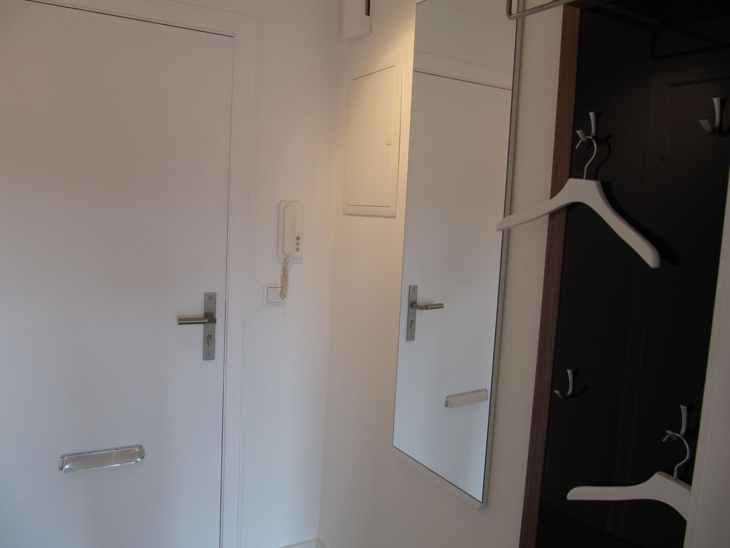 Ein Badezimmer mit weißer Tür, einem Spiegel, einem Handtuchhalter und einem Waschbecken.