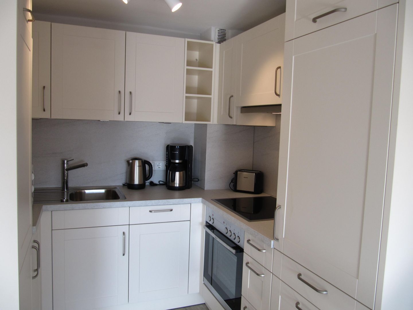A compact kitchen with white cabinets, a built-in oven, a coffee maker, and a toaster.