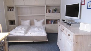 Une chambre à coucher comprenant un lit, un bureau, une télévision et des étagères intégrées où sont rangés des livres et des objets décoratifs.
