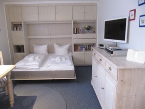 Un dormitorio con cama, escritorio, televisor y estanterías empotradas con libros y objetos decorativos.