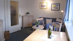 Een gezellige woonkamer met een bank, een klein rond tafeltje en een fles wijn op een vloermat.