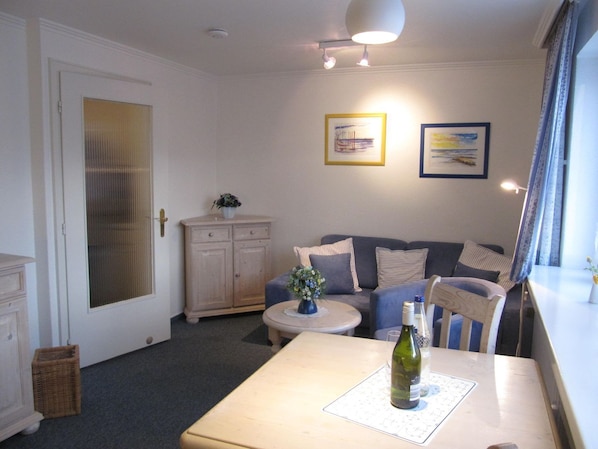 A cozy living room with a sofa, a small round table, and a bottle of wine on a mat.