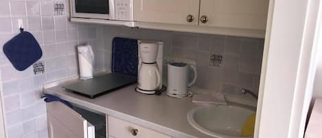 Eine kompakte Küche mit Mikrowelle, Kaffeemaschine und Spüle.