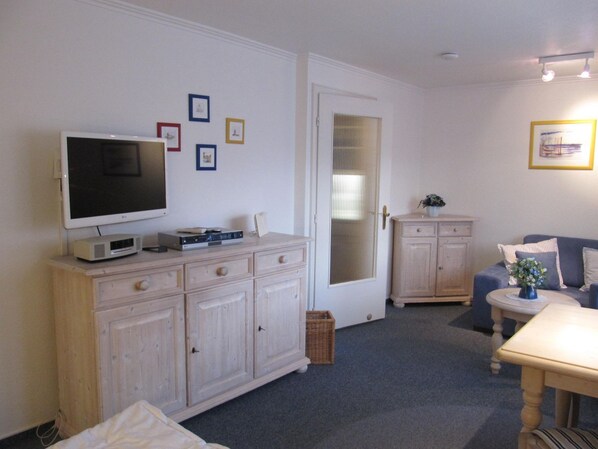 Ein Wohnzimmer mit Fernseher, Schrank und einer Couch.
