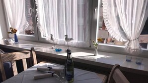 Un coin repas avec une table dressée pour deux personnes, une bouteille d’eau et un vase rempli de fleurs.