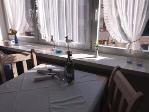 Un comedor con una mesa preparada para dos, una botella de agua y un florero con flores.