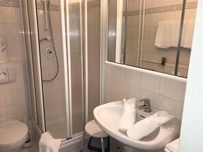 Un baño con ducha de vidrio, lavamanos con espejo y retrete.