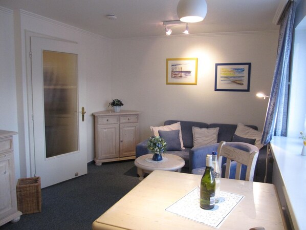 A cozy living room with a sofa, a small round table, and a bottle of wine on a mat. - Apartment at Andreas-Dirks-Str. 1, Apartment 103 - 1-room apartment in the (Sylt)