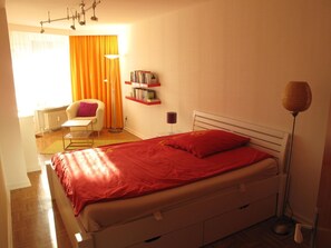 Una camera da letto con un letto, una sedia, una lampada da terra e una libreria.