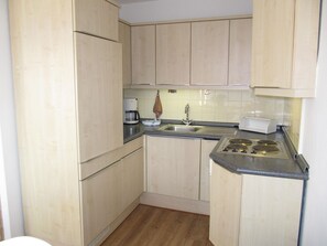 A compact kitchen with wooden cabinets, a sink, a coffee maker, and a stove.